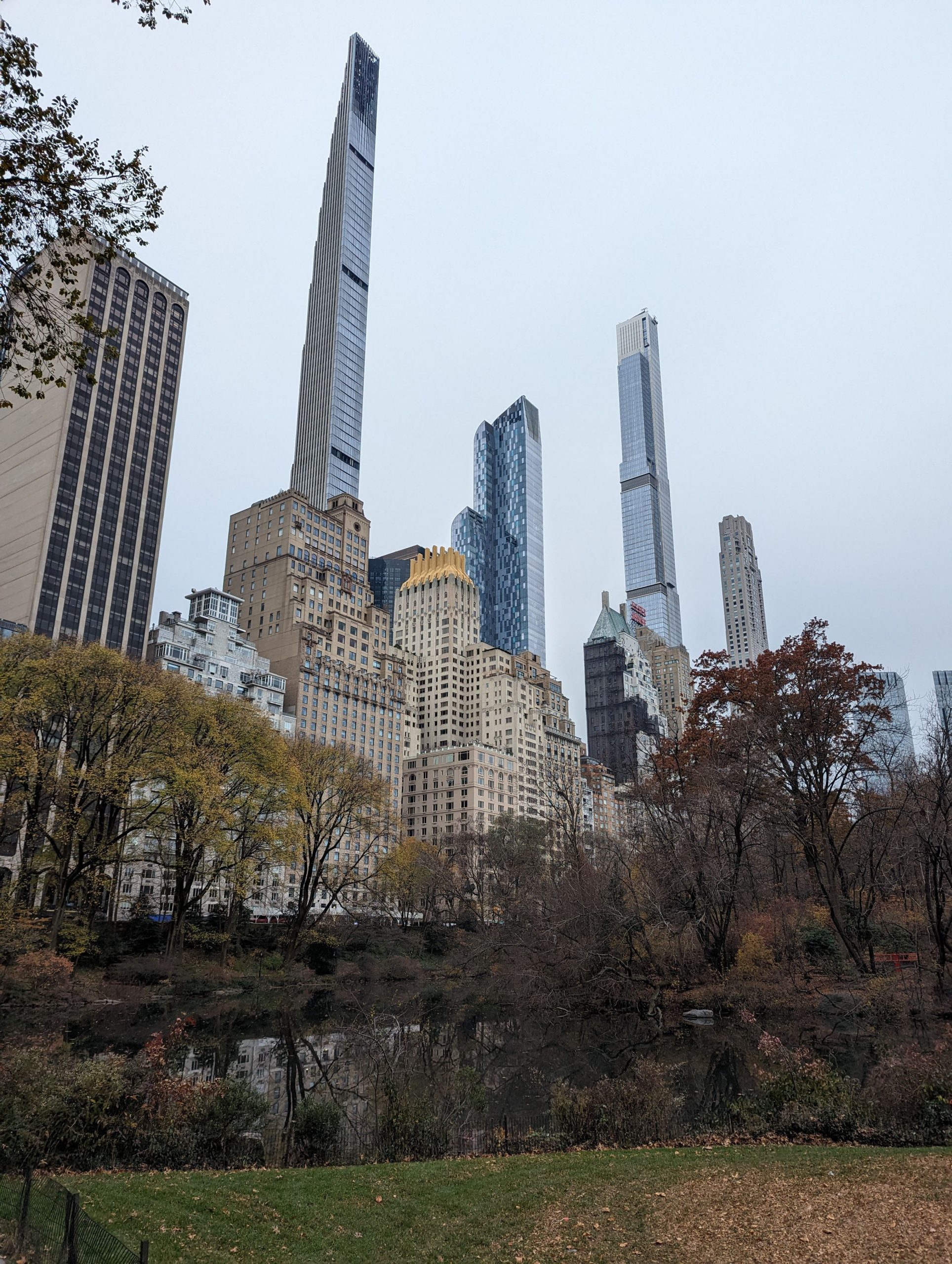 City skyline with tall modern skyscrapers rising above a tree-lined park in autumn hues.