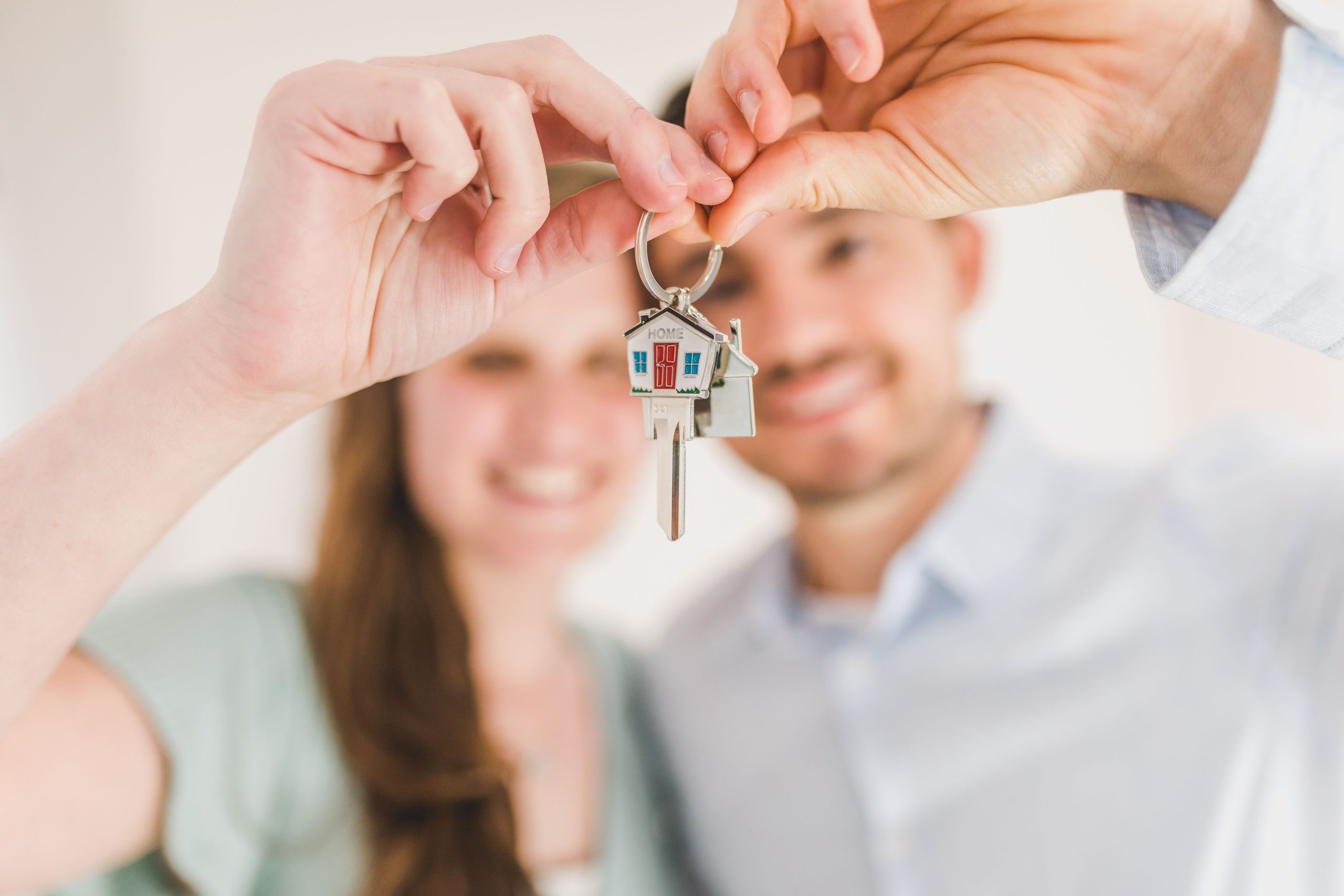 Couple holding up a house-shaped keychain together, symbolizing home ownership.
